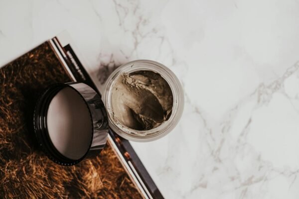 High-angle view of a clay mask in a glass jar on a marble surface with a magazine.
